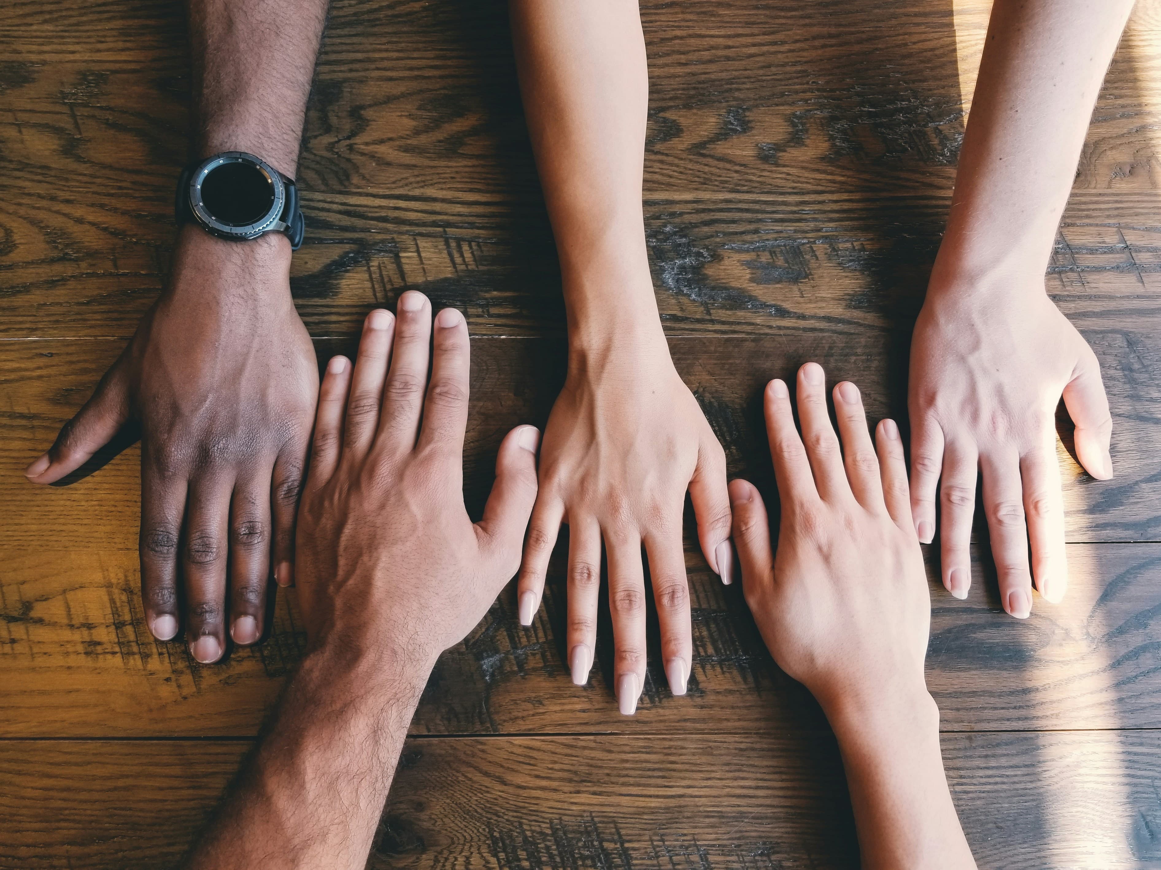 A group of hands resting together on a wooden table